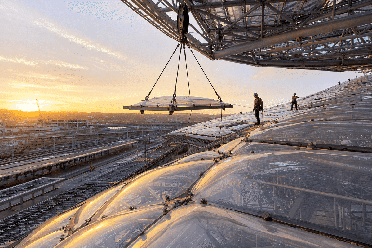 Construction crew installing ETFE cushion modules on a railway station roof grid