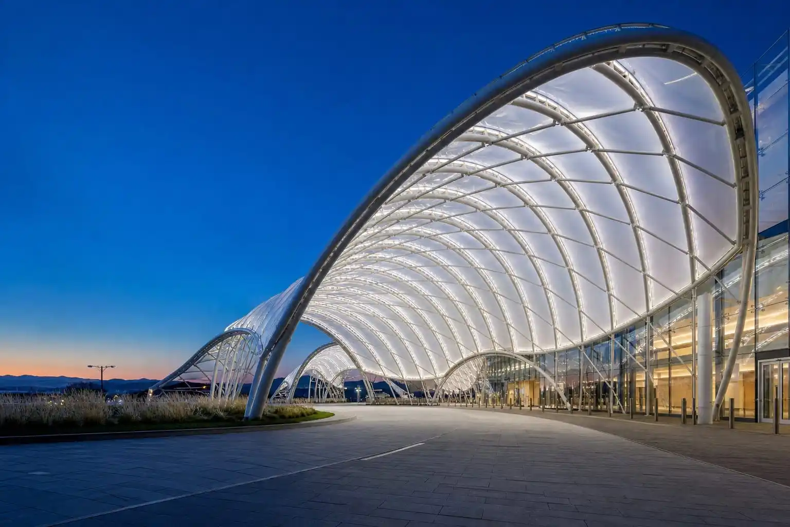 Glowing translucent ETFE film canopy on curved steel structure at dusk